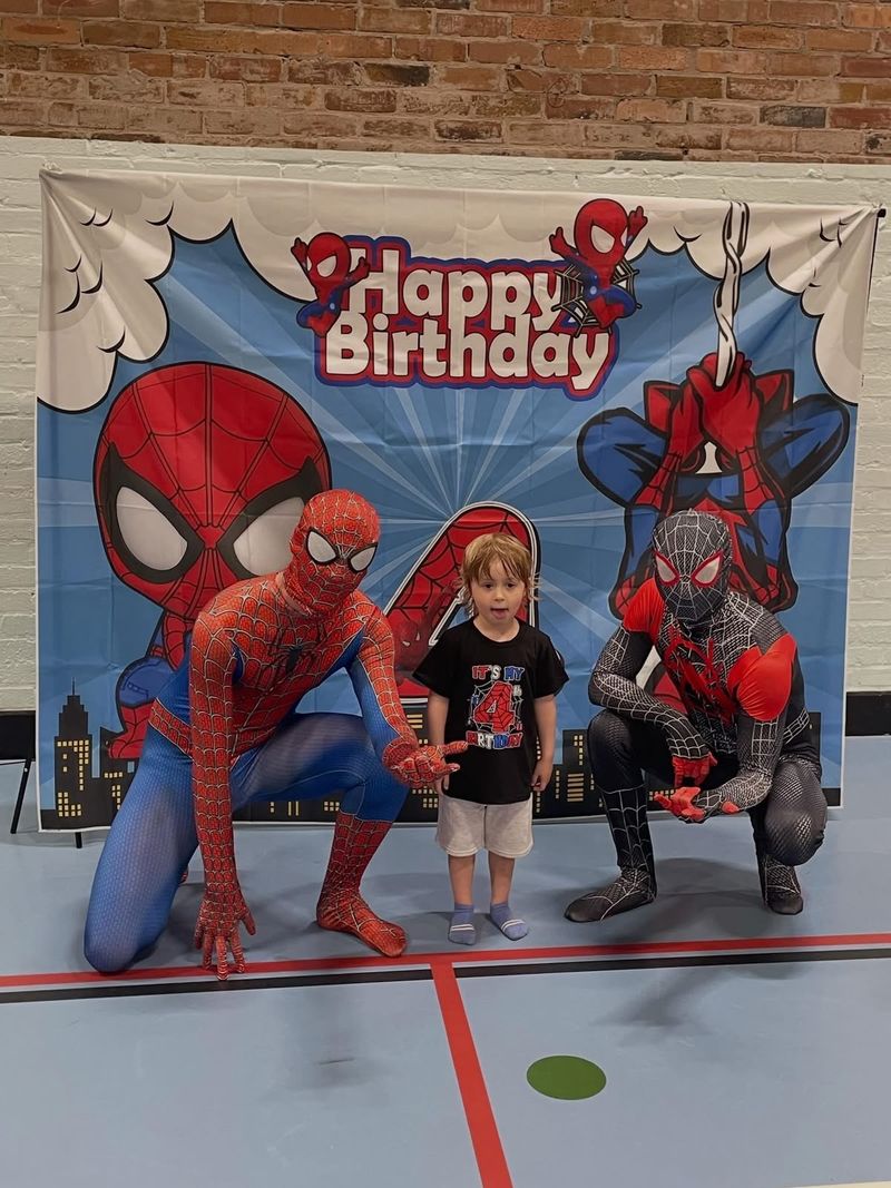 Two superhero look-alikes with the birthday boy in front of a Happy Birthday banner