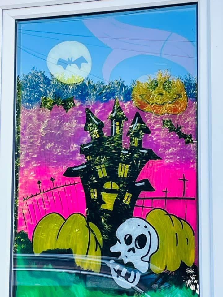A haunted house with pumpkins, a skull and bats, painted on a window for Halloween
