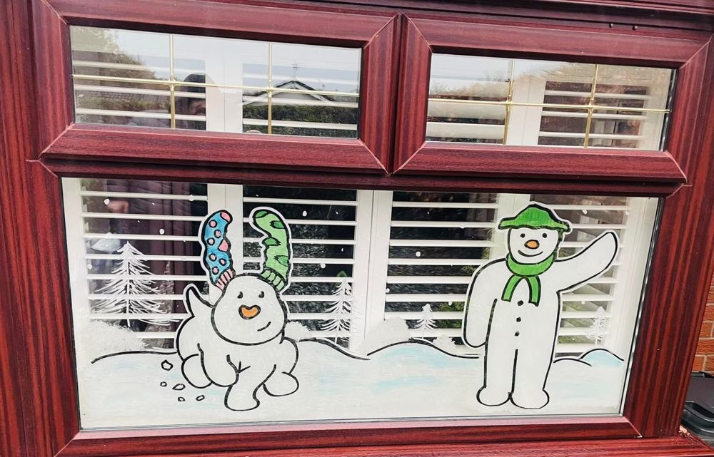 A snowman and his dog in a snowy scene, painted on a window